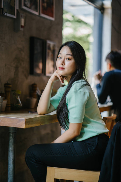 Portrait of a young and attractive Chinese Asian woman lounging and relaxing at a cafe during the day on a weekend. She is wearing a mint green sweater - Foto, Bild