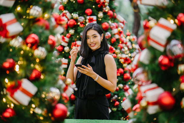 Portrait of a beautiful and young Korean Asian woman smiling as she beholds and marvels at the Christmas decorations - Valokuva, kuva