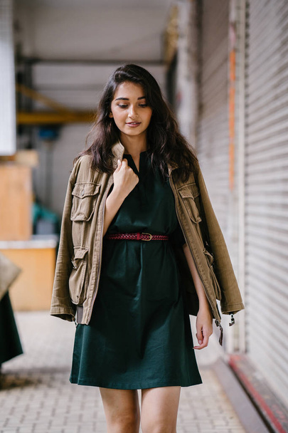 young, tall, slim and elegant Indian Asian woman poses for a portrait. She is wearing comfortable and stylish casual clothing and has a man's jacket draped over her shoulders.  - 写真・画像