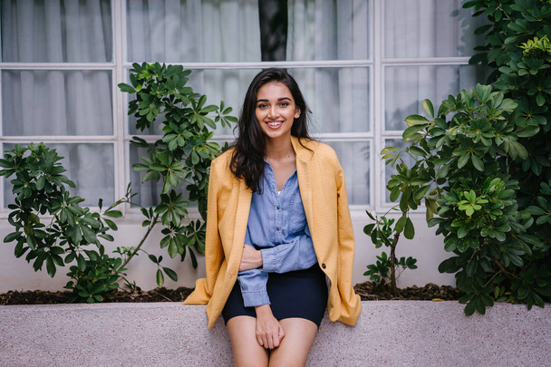 Fashionable, elegant and young Indian Asian woman in a retro outfit. She is wearing a yellow jacket draped over a comfortable summer outfit. - Fotó, kép