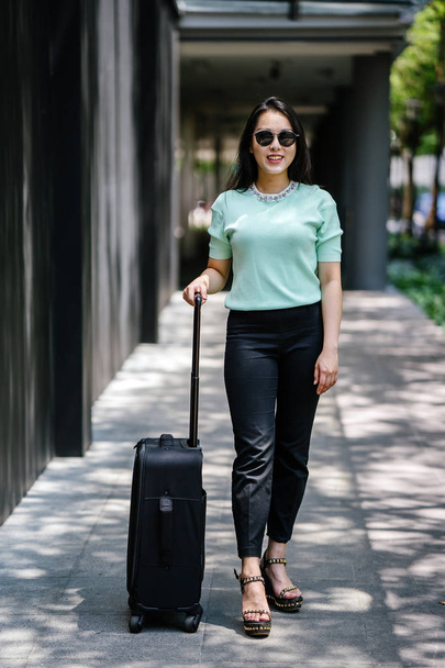 A young Asian woman is pulling her suitcase luggage. She is attractive, elegant and fashionably dressed - 写真・画像