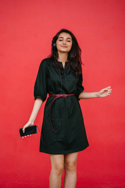 Studio portrait of a beautiful, young and attractive Indian Asian woman in a green dress and red belt against a red background - Foto, afbeelding