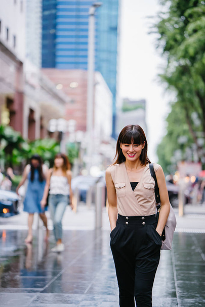 young Chinese Asian woman standing outside a mall in Asia with shopping malls in the background - 写真・画像