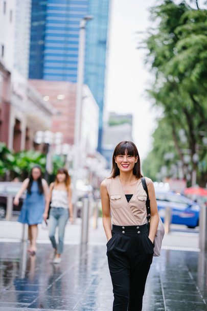 young Chinese Asian woman standing outside a mall in Asia with shopping malls in the background - 写真・画像