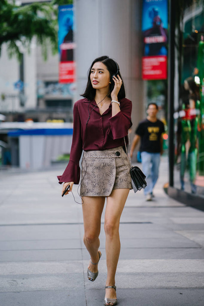 beautiful Korean woman in an elegant blouse and shorts dancing as she walks down a street in the city with her headphones on - Fotoğraf, Görsel