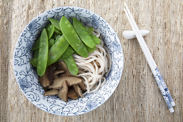 Filling bowl with udon noodle soup series image four: bowl withnoodles, shiitake mushrooms, and snow peas. - Photo, image