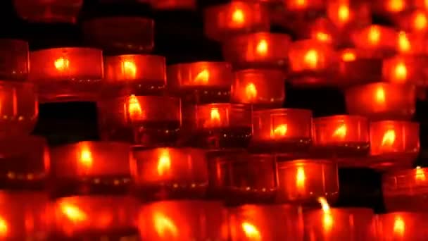 Égő gyertyák memorial a katolikus egyház. Sorban a keresztény imádság piros kerek fogadalmi gyertya éget a sötétben. Gyertyagyújtás az áldozati imádság zár-megjelöl kilátás. Ünneplő karácsony-székesegyház - Felvétel, videó