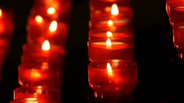 Sorban a keresztény imádság piros kerek fogadalmi gyertya éget a sötétben. Gyertyagyújtás az áldozati imádság közelről. Égő gyertyák memorial a katolikus egyház. Ünneplő karácsony-székesegyház - Felvétel, videó