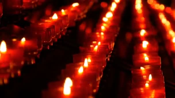 Sorban a keresztény imádság piros kerek fogadalmi gyertya éget a sötétben. Gyertyagyújtás az áldozati imádság zár-megjelöl kilátás. Égő gyertyák memorial a katolikus egyház. Ünneplő karácsony-székesegyház - Felvétel, videó