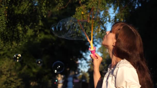 Girl blows big soap bubbles and laughs while walking in park. Summer walks and games in nature - Footage, Video