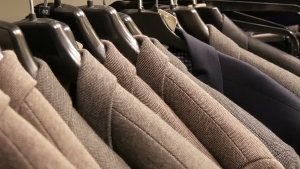 Szeregu ciepłe kurtki na wieszaku w sklepie Odzież męska w centrum handlowym. Garnitury męskie różne wiszące w centrum handlowym - Materiał filmowy, wideo