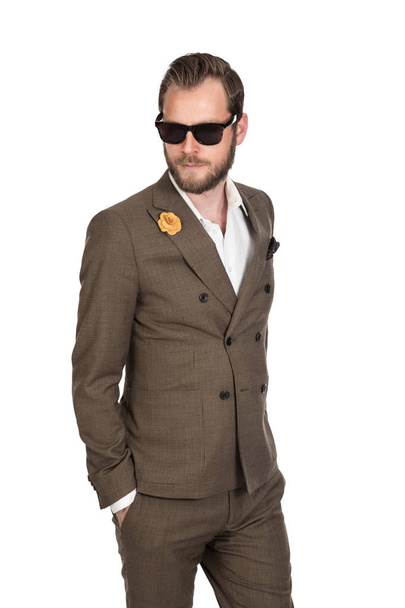Cool trendy businessman in a brown suit, white shirt and sunglasses walking against a white background with a focused tough look. - Foto, Imagem