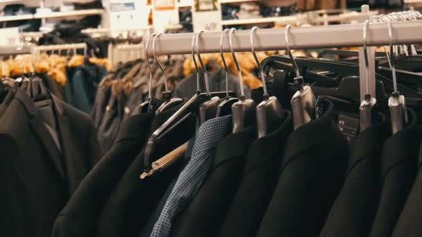 Szeregu ciepłe kurtki na wieszaku w sklepie Odzież męska w centrum handlowym. Garnitury męskie różne wiszące w centrum handlowym - Materiał filmowy, wideo