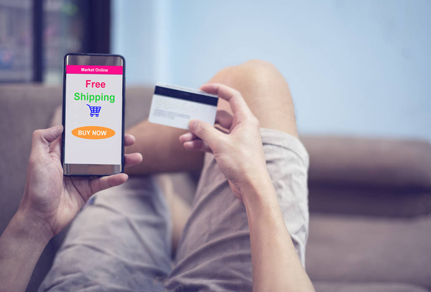 koncepcja zakupy online - młody człowiek za pomocą smartphone zakupy w witrynie rynku online i ręce trzyma karty kredytowej na łóżku - komfortowe relaks szczęśliwy zakupy online wakacje w domu - Zdjęcie, obraz