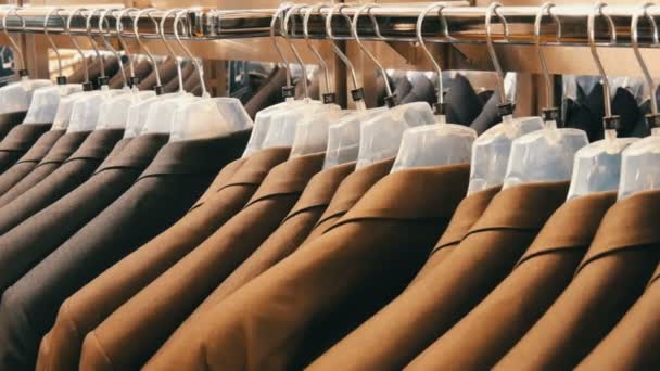 Коричневые и серые мужские куртки висят на вешалках в магазине мужской одежды в торговом центре. Огромный выбор мужских костюмов на вешалках в торговом центре вблизи
 - Кадры, видео