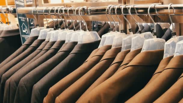 Im Herrenbekleidungsgeschäft im Einkaufszentrum hängen braune und graue Herrenjacken an Kleiderbügeln. eine riesige Auswahl an Herrenanzügen auf Kleiderbügeln in Einkaufszentrum Nahaufnahme - Filmmaterial, Video