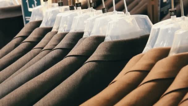 Im Herrenbekleidungsgeschäft im Einkaufszentrum hängen braune und graue Herrenjacken an Kleiderbügeln. eine riesige Auswahl an Herrenanzügen auf Kleiderbügeln in Einkaufszentrum Nahaufnahme - Filmmaterial, Video