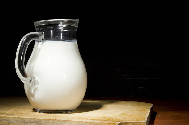 Glass jug with fresh milk on a wooden table - Fotoğraf, Görsel