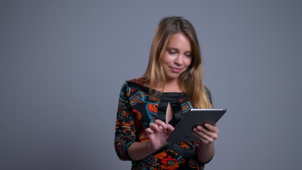 Closeup portrait of attractive young caucasian female scrolling on the tablet looking at camera and laughing - Imágenes, Vídeo