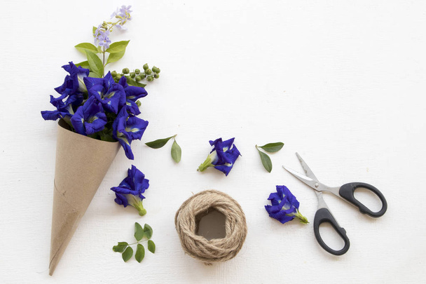  fleur bleue papillon pois herbes flore locale de l'Asie arrangement en cône de papier et ciseaux à corde sur fond blanc en bois
 - Photo, image
