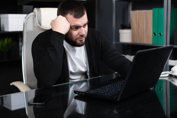 Retrato do jovem homem apoiando a cabeça com o punho com laptop no escritório de negócios
 - Foto, Imagem