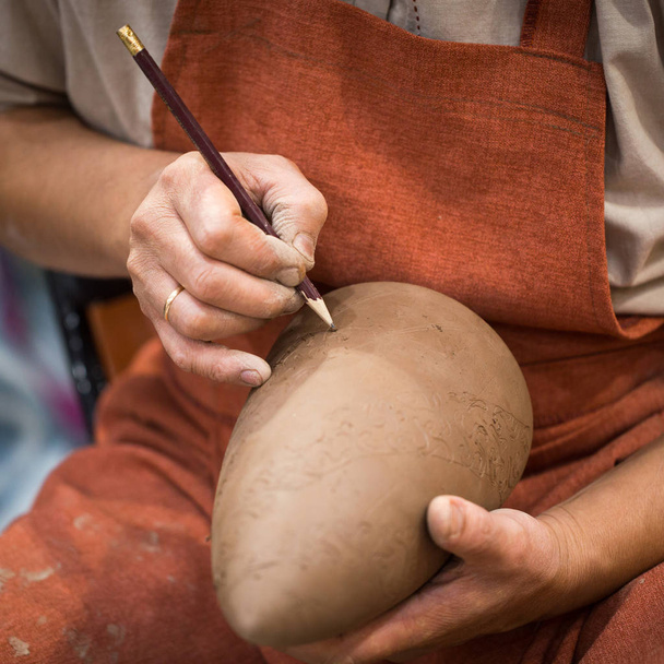 In der Keramikwerkstatt stellt der Meister eine Keramikkanne auf ungebranntes Steingut. Großaufnahme der Meisterhände. Handarbeit, ein Hobby. Hintergrund veranschaulicht die manuelle Arbeit mit Ton. - Foto, Bild