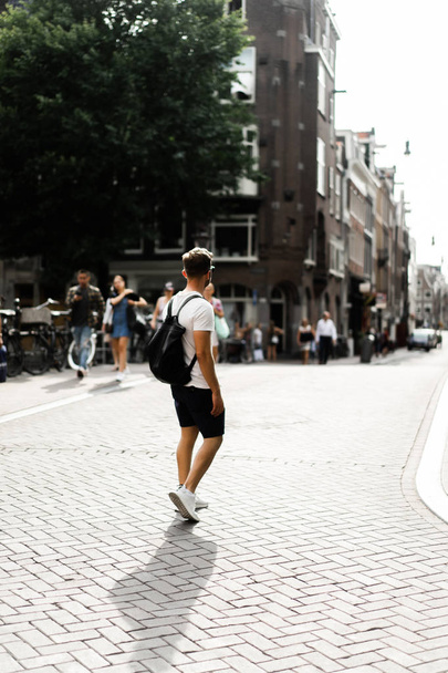 Człowiek z plecakiem idzie ulicami Amsterdamu. - Zdjęcie, obraz