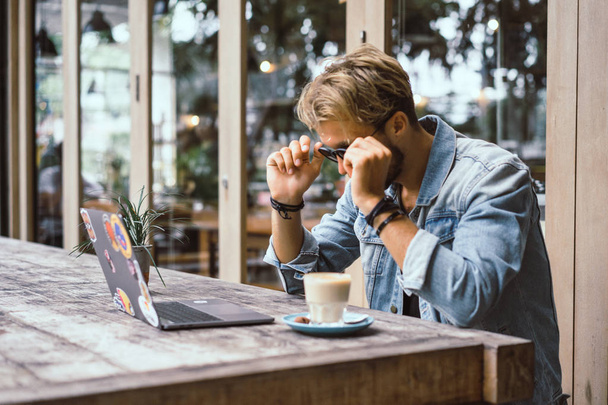 young attractive business man in a cafe works for a laptop, drinks coffee. - Photo, Image