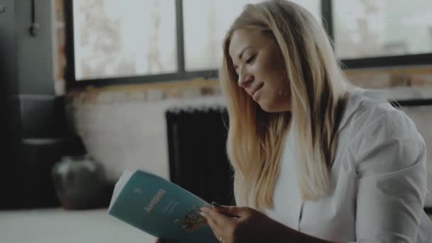 Portrait young woman reading interesting book while relaxing in the living room. - Materiał filmowy, wideo
