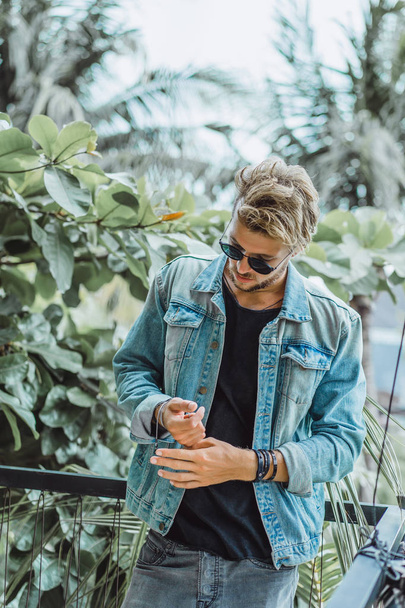 young attractive man posing in a tropical location, on a background of palm trees and greenery, in sunglasses - Zdjęcie, obraz