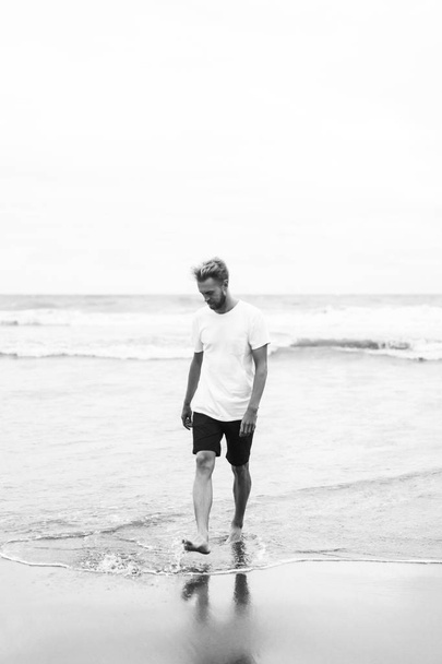 young attractive man walking along the ocean beach on a sandy beach - Фото, изображение