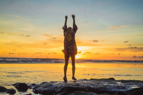 people on the beach at sunset. the girl is jumping against the backdrop of the setting sun. - Foto, imagen