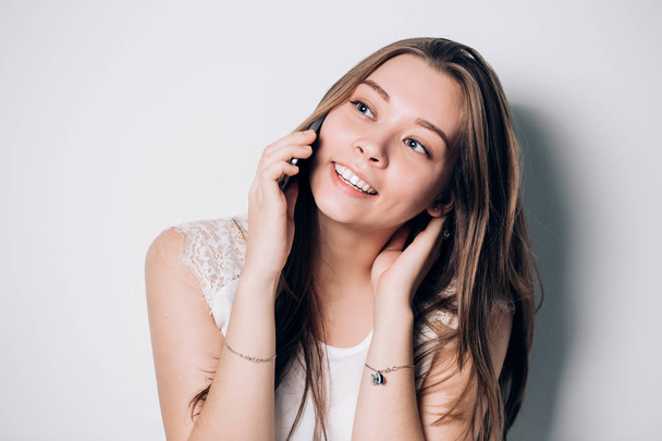 Nuori nainen puhuu puhelimessa valkoisella taustalla. Hauska kaunis hymyilevä tyttö. Positiiviset tunteet, onnellisuus, ilo, verkkokaupoissa käsite
 - Valokuva, kuva
