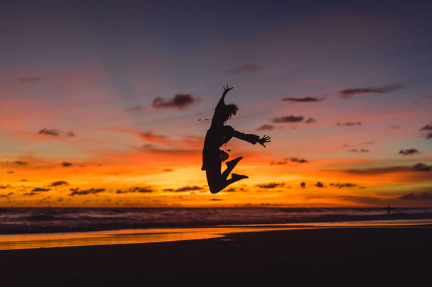 people on the beach at sunset. the girl is jumping against the backdrop of the setting sun. - Zdjęcie, obraz