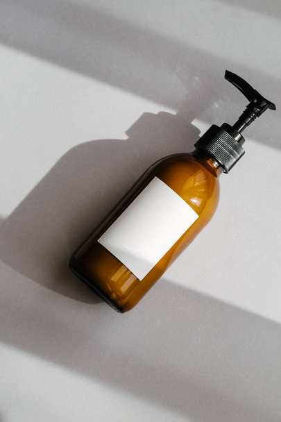 One pump dispenser glass brown bottle for cosmetics, white label with space for text, overhead. Direct light. Beauty blogging, salon treatment, minimalism concept - Photo, Image