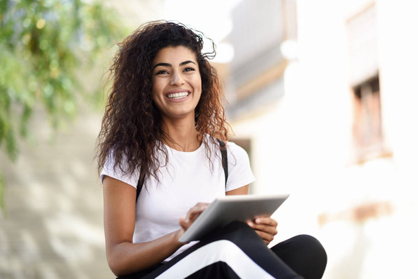 Smiling African woman using digital tablet outdoors. Happy Arab girl wearing sportswear and smiling in urban background - Photo, Image