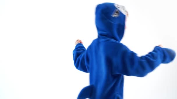 alegre niño bailando divertido sobre un fondo blanco en pijama kigurumi, traje de tiburón azul
 - Metraje, vídeo