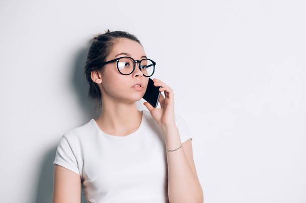 Young beautiful woman talking on phone in office against a light gray background with copy space - Foto, immagini