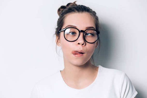Close up indoor fashion lifestyle portrait of cool pretty young brunette girl, amazing. making crazy funny grimace in glasses on a white background - Фото, изображение