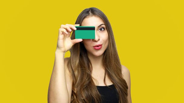 Retrato de una hermosa joven con tarjeta de crédito en la cara aislada sobre fondo amarillo
 - Foto, imagen