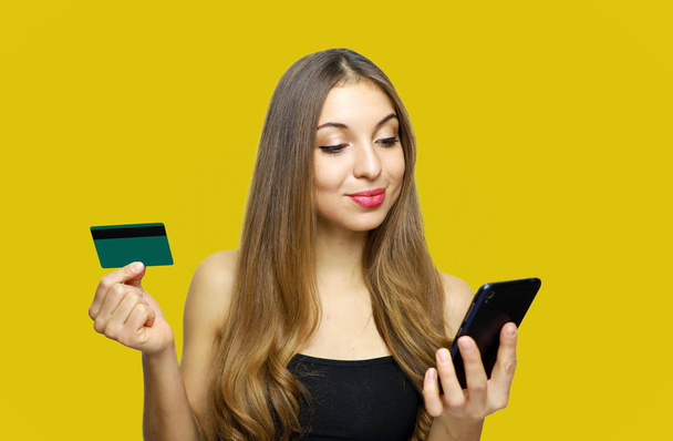 Obraz uśmiechający się Pani młody na białym tle nad żółtym tle przy użyciu telefonu komórkowego z posiadania karty kredytowej - Zdjęcie, obraz
