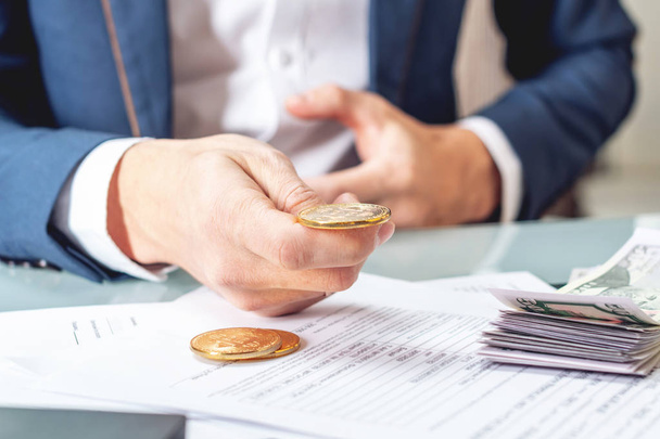 Üzletember bankár holding egy érme bitcoin papírokkal az asztalnál ül. A koncepció cseréje és eladása a dollár cryptocurrency - Fotó, kép
