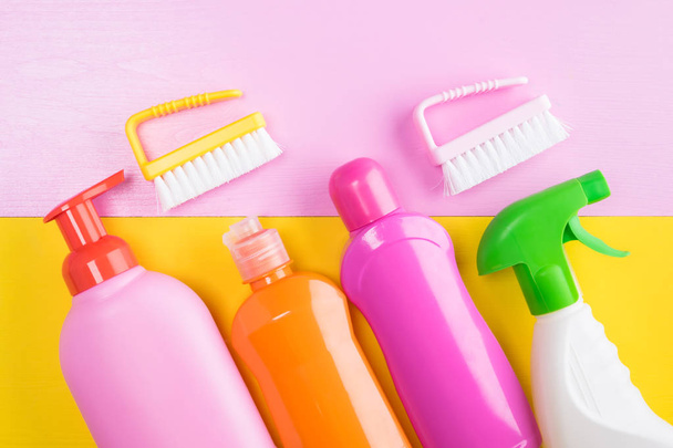 concetto da bottiglie colorate con prodotti per la pulizia e pennelli per la pulizia su sfondo rosa-giallo
 - Foto, immagini