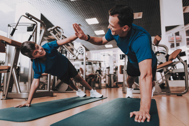 Young Father and Son Doing Exercises in Sport Club. Healthy Lifestyle Concept. Sport and Training Concepts. Modern Sport Club. Sport Equipment. Family Sport. Running Tracks. Parent with Child. - Photo, image