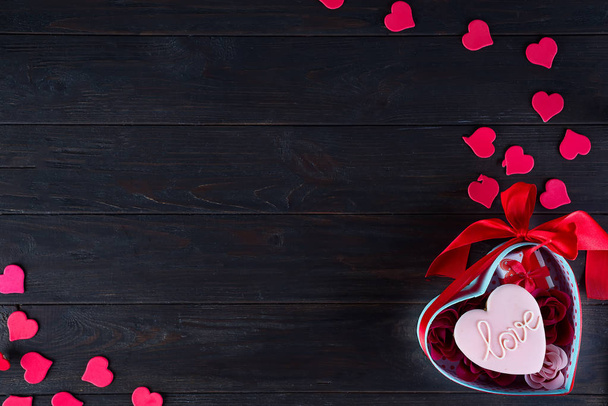 Süßigkeiten am Valentinstag. Kekse in Herzform und Schriftzug Liebe, rote Herzen in Form und Strauß Rose in Geschenkbox auf dunklem Holzhintergrund Draufsicht - Foto, Bild
