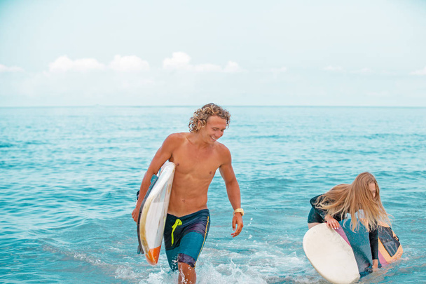 Surfistas na praia- casal sorridente de surfistas andando na praia e se divertindo no verão. Conceito de esporte e férias extremas
 - Foto, Imagem