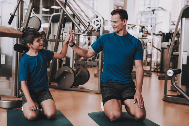 Young Father and Son Doing Exercises in Sport Club. Healthy Lifestyle Concept. Sport and Training Concepts. Modern Sport Club. Sport Equipment. Family Sport. Running Tracks. Parent with Child. - 写真・画像