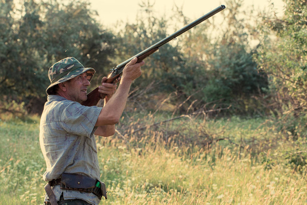 Jagdzeit, Herbstsaison geöffnet. Ein Jäger mit einem Gewehr in der Hand in Jagdkleidung im herbstlichen Wald auf der Suche nach einer Trophäe. - Foto, Bild