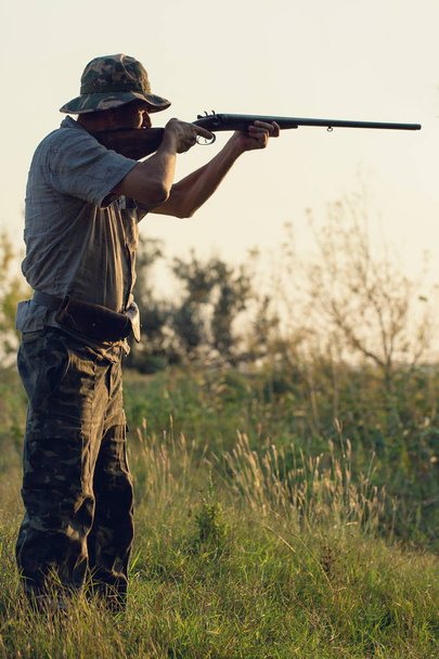 Período de caza, temporada de otoño abierta. Un cazador con un arma en sus manos en ropa de caza en el bosque de otoño en busca de un trofeo
. - Foto, imagen