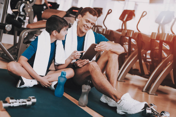 Young Father and Son Sitting on Mats in Sport Club. Healthy Lifestyle Concept. Sport and Training Concepts. Modern Sport Club. Sport Equipment. Family Sport. Rest after Training. Parent with Child. - Photo, Image